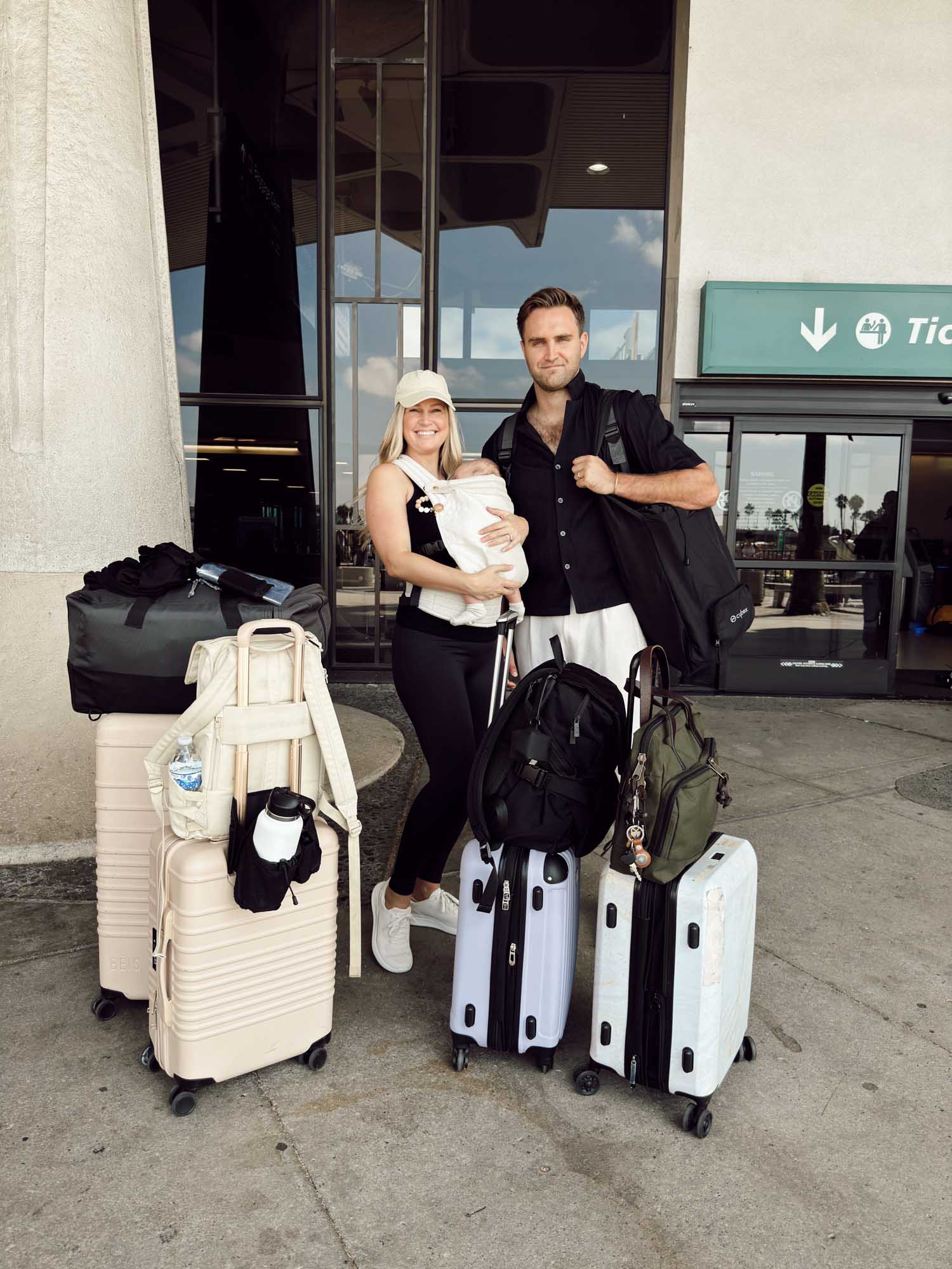 couple with newborn baby taking first flight with lots of luggage outside of the airport