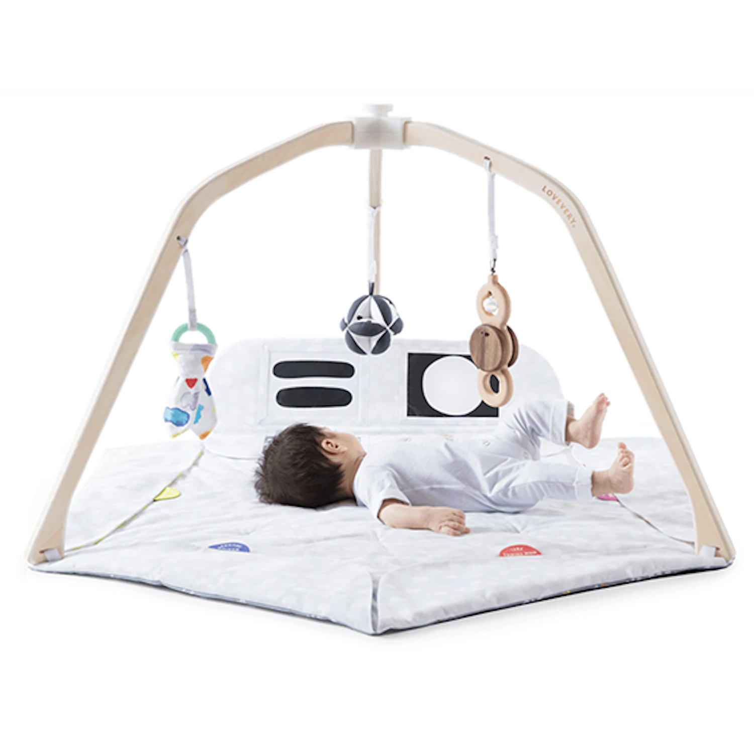 baby dressed in white on mat with beige play set above them with colorful mobile toys hanging from above