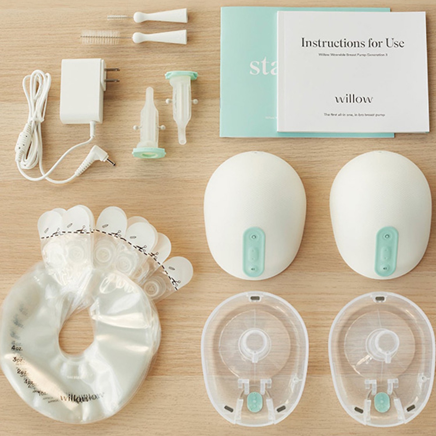 Product image of breast pump and accessories on wooden table including the chargers, cleaning supplies, bags, and instruction manual