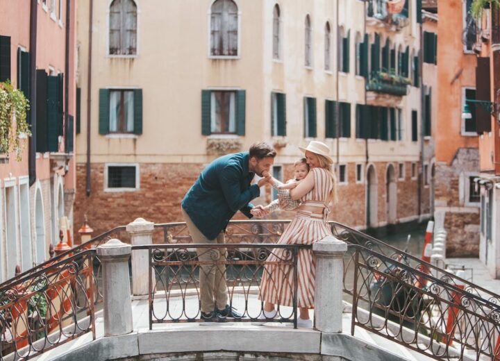 brunette man in blue blazer kissing baby's foot that woman in striped dress is holding with Venice canals of Italy in background