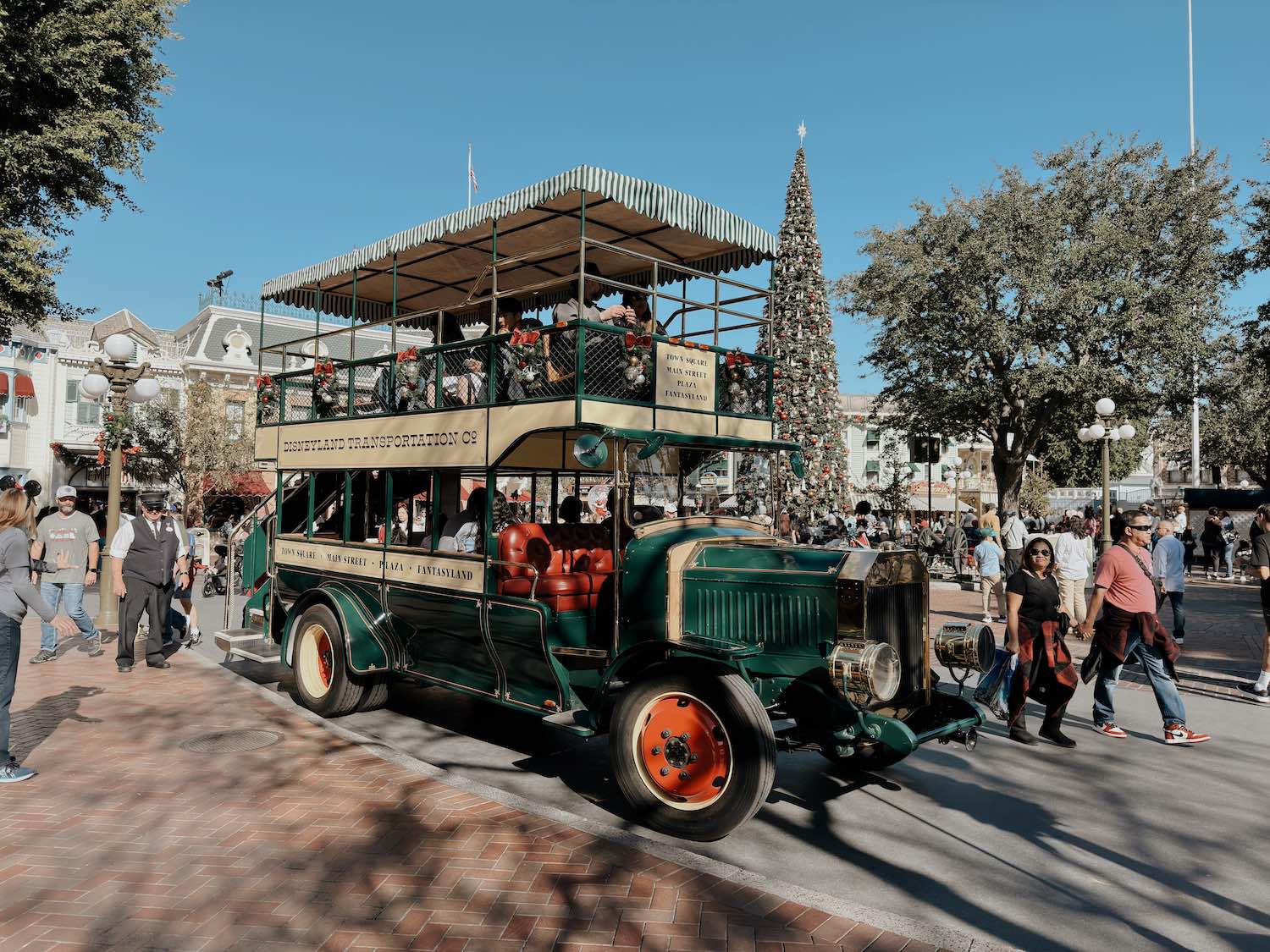 Old 20th century double decker automobile in green with red rims on Main Street in Disneyland with tall Christmas tree in the background