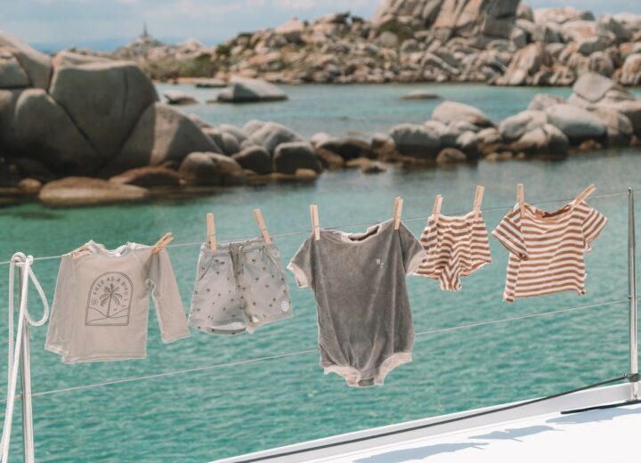 Toddler clothes hanging on a yacht line with clothes pins with clear blue waters and rocks on the horizon in the background