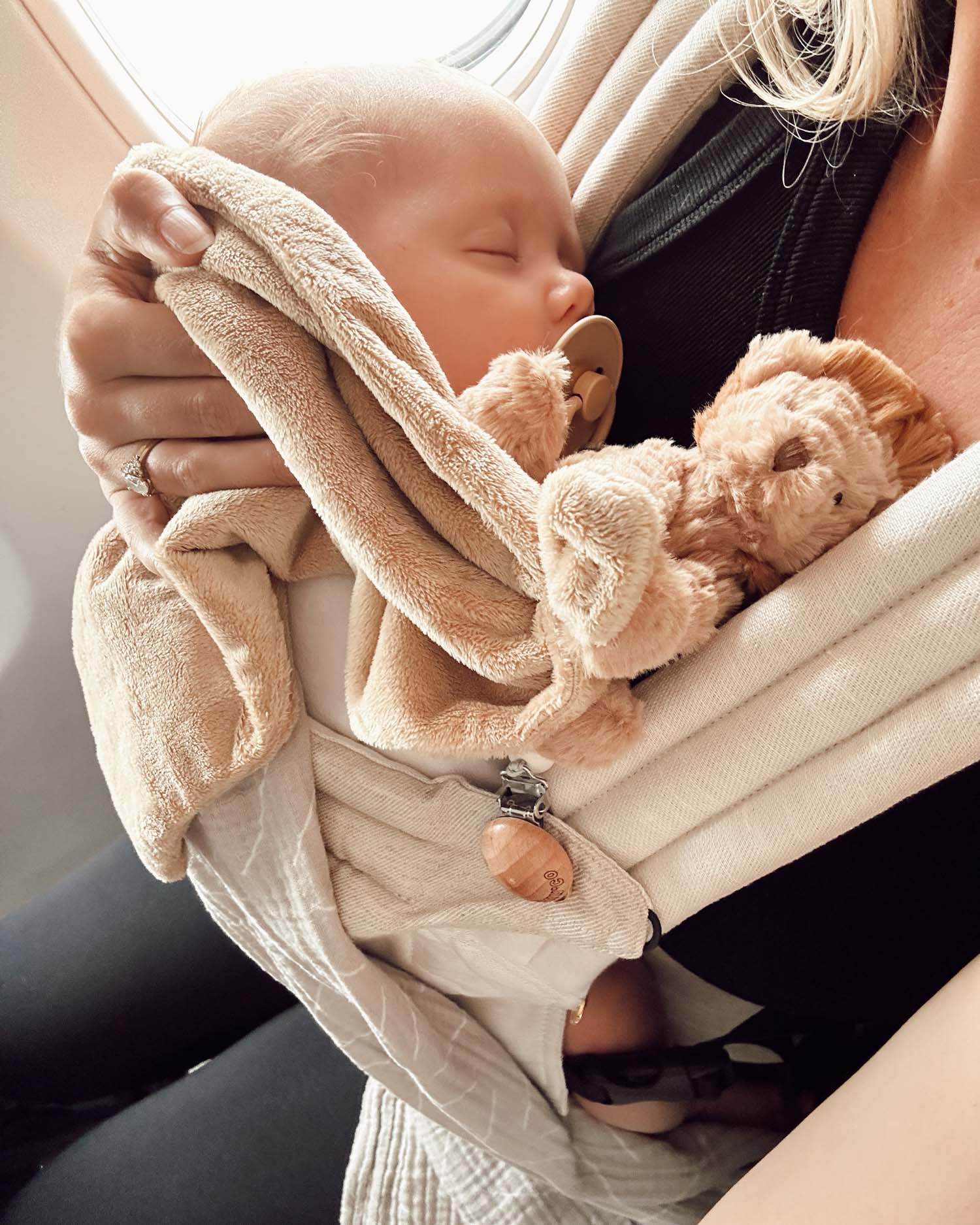 baby asleep in carrier with lion lovey with pacifier in window seat on plane