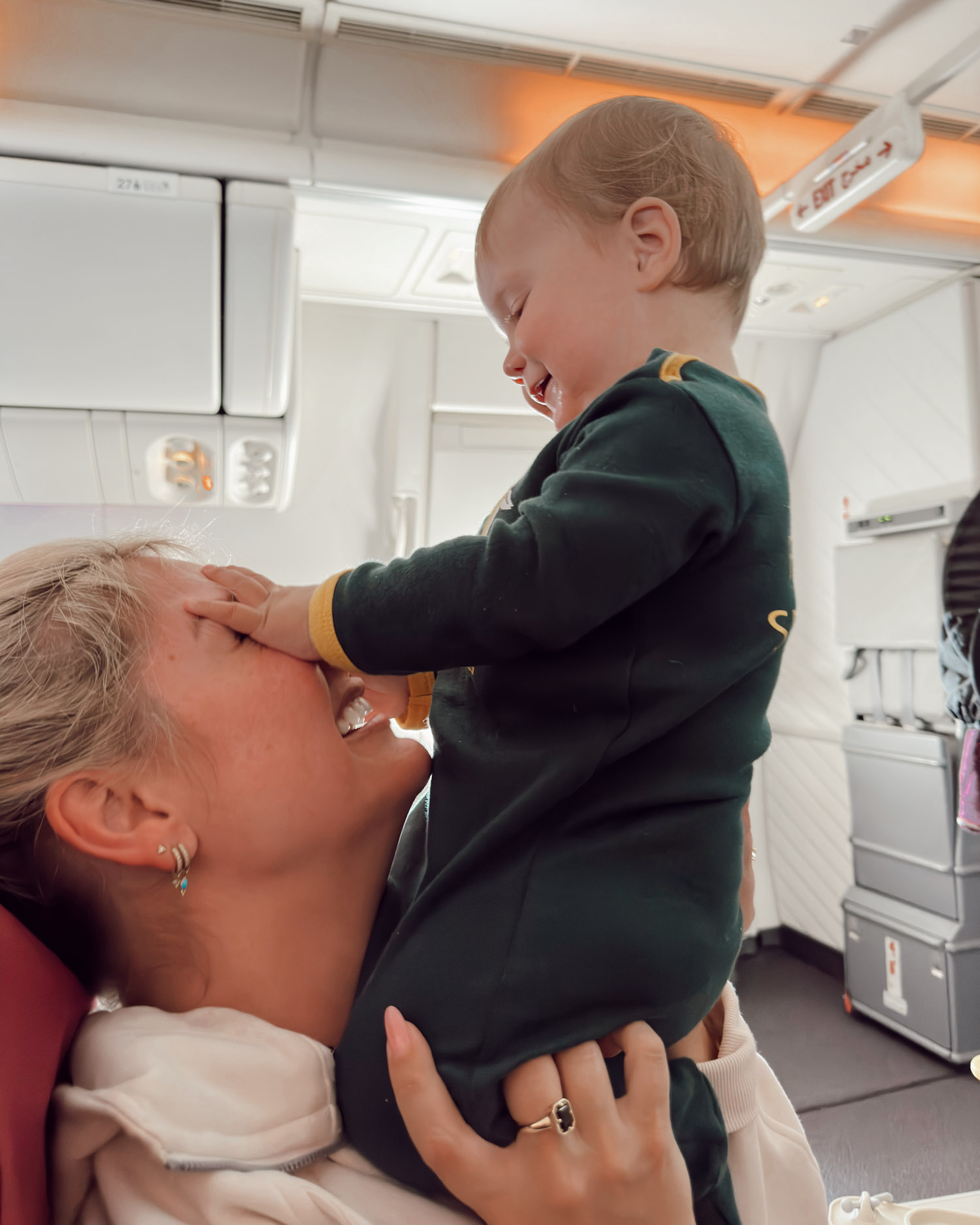 baby playing with mom on airplane in economy seat laughing