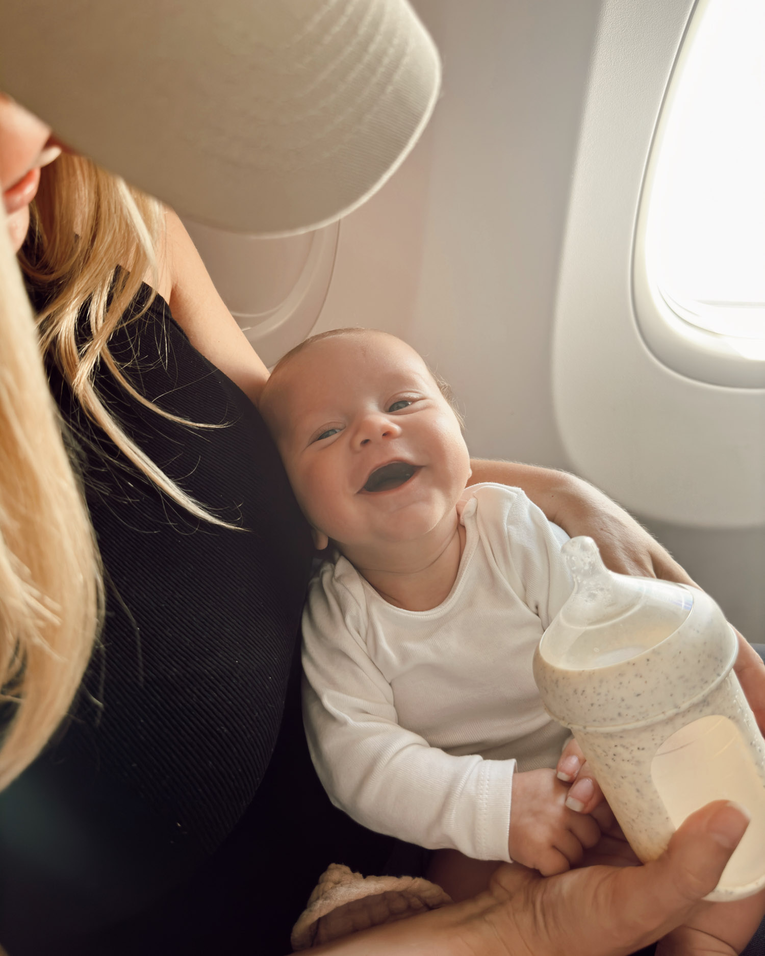 infant first flight on plane with mom in window seat drinking baby bottle