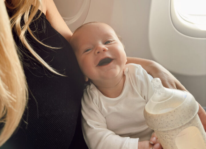 infant first flight on plane with mom in window seat drinking baby bottle