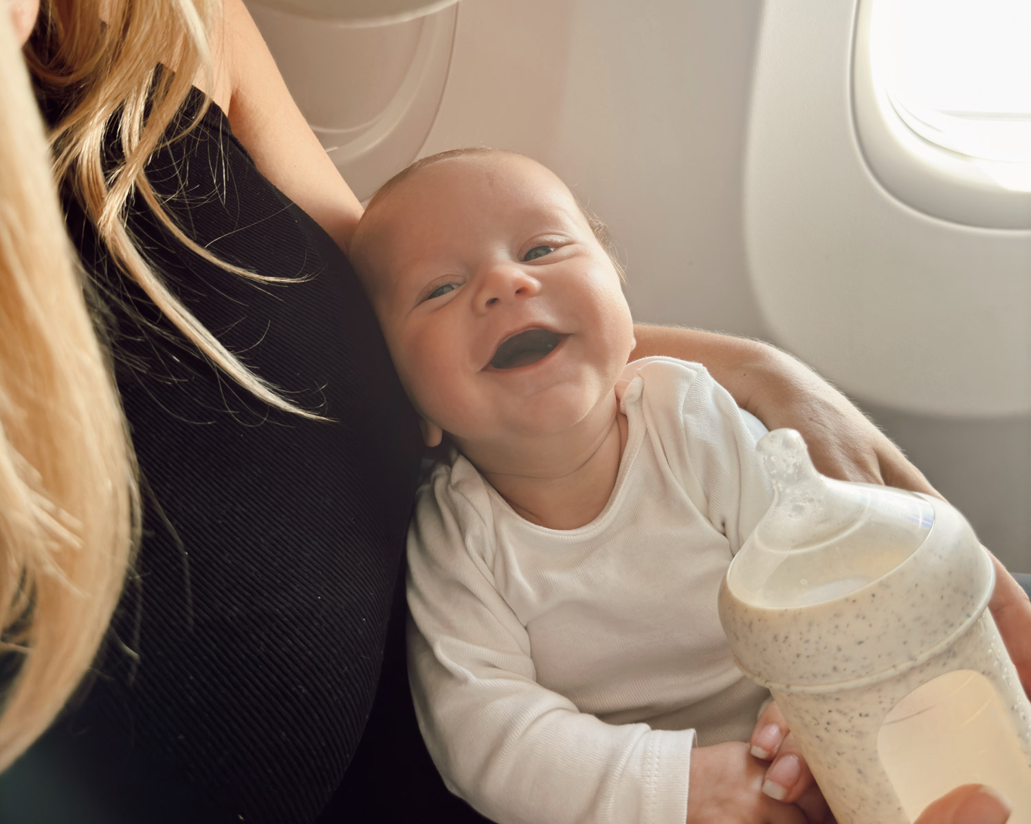 infant first flight on plane with mom in window seat drinking baby bottle