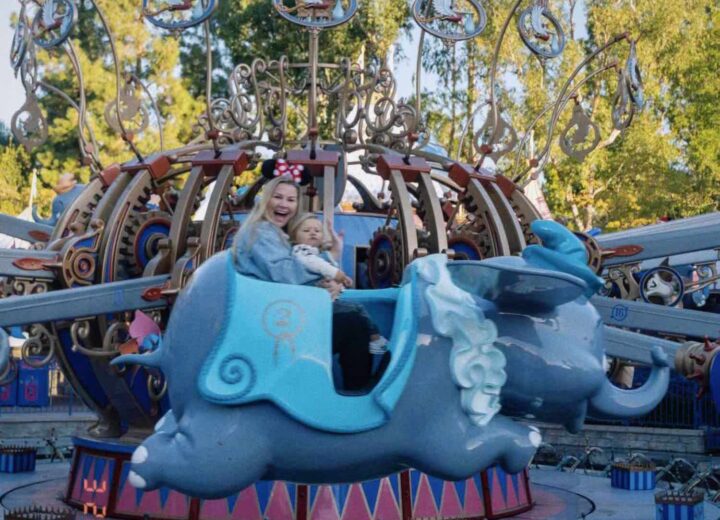 Dumbo ride at Disneyland mid-flight with a slightly blurry blonde woman smiling at camera holding toddler in lap