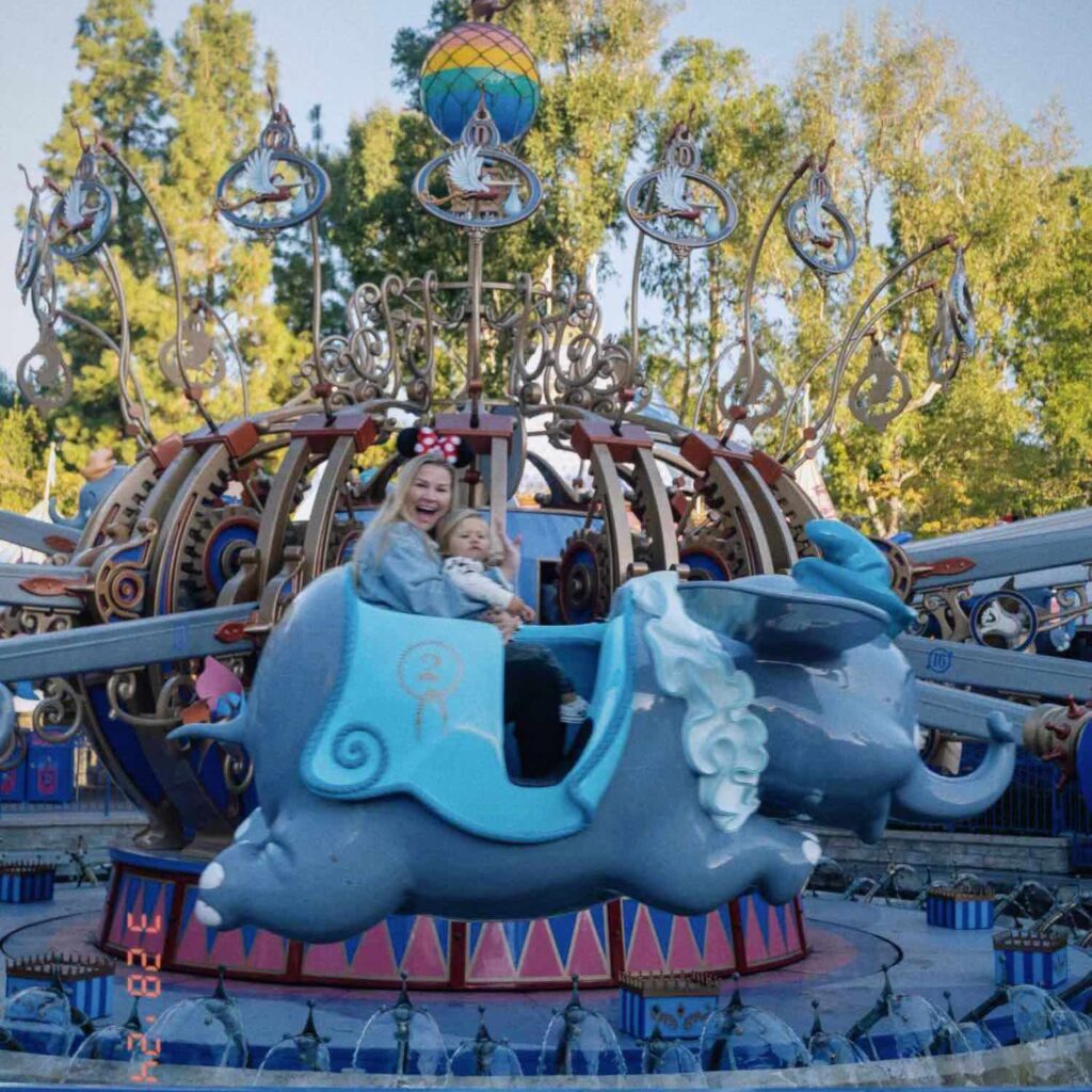 Dumbo ride at Disneyland mid-flight with a slightly blurry blonde woman smiling at camera holding toddler in lap