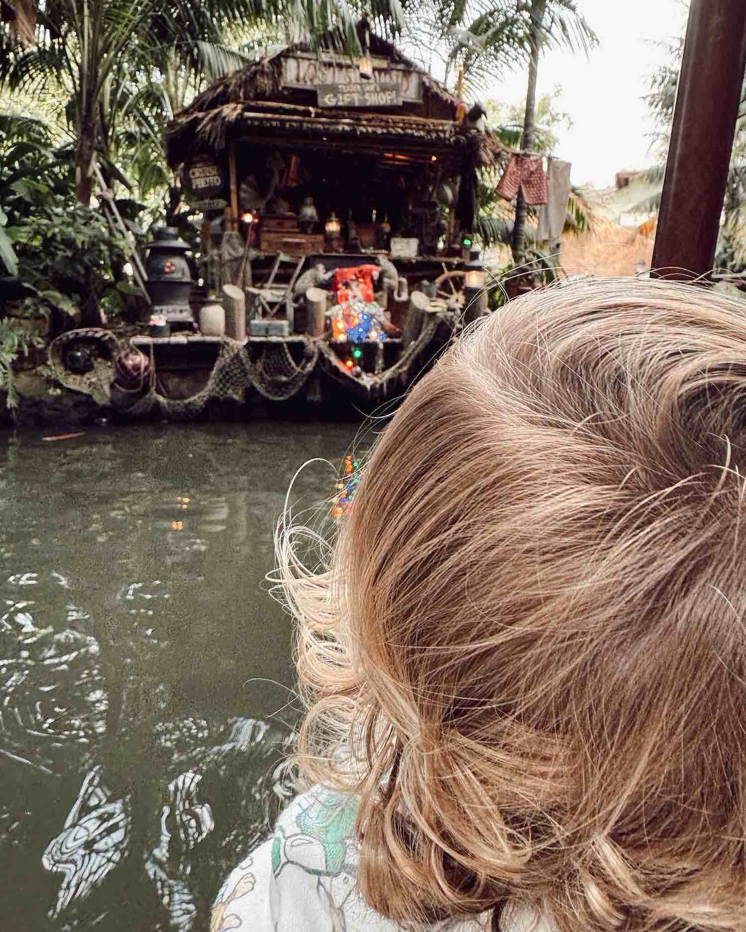 Back of toddler's head showing blond curls with tropical, cabin on green water with palms