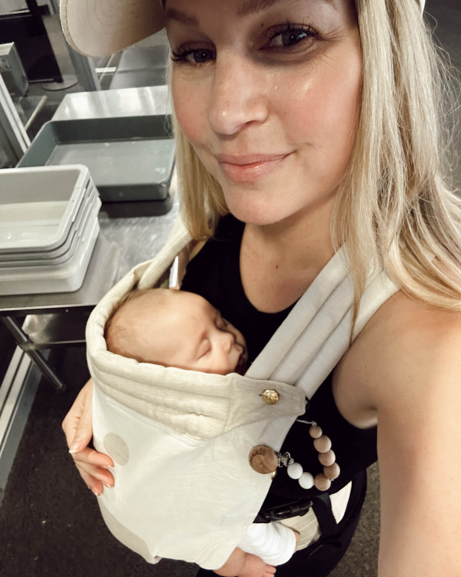 blonde mom in hat wearing sleeping baby in baby carrier through airport security