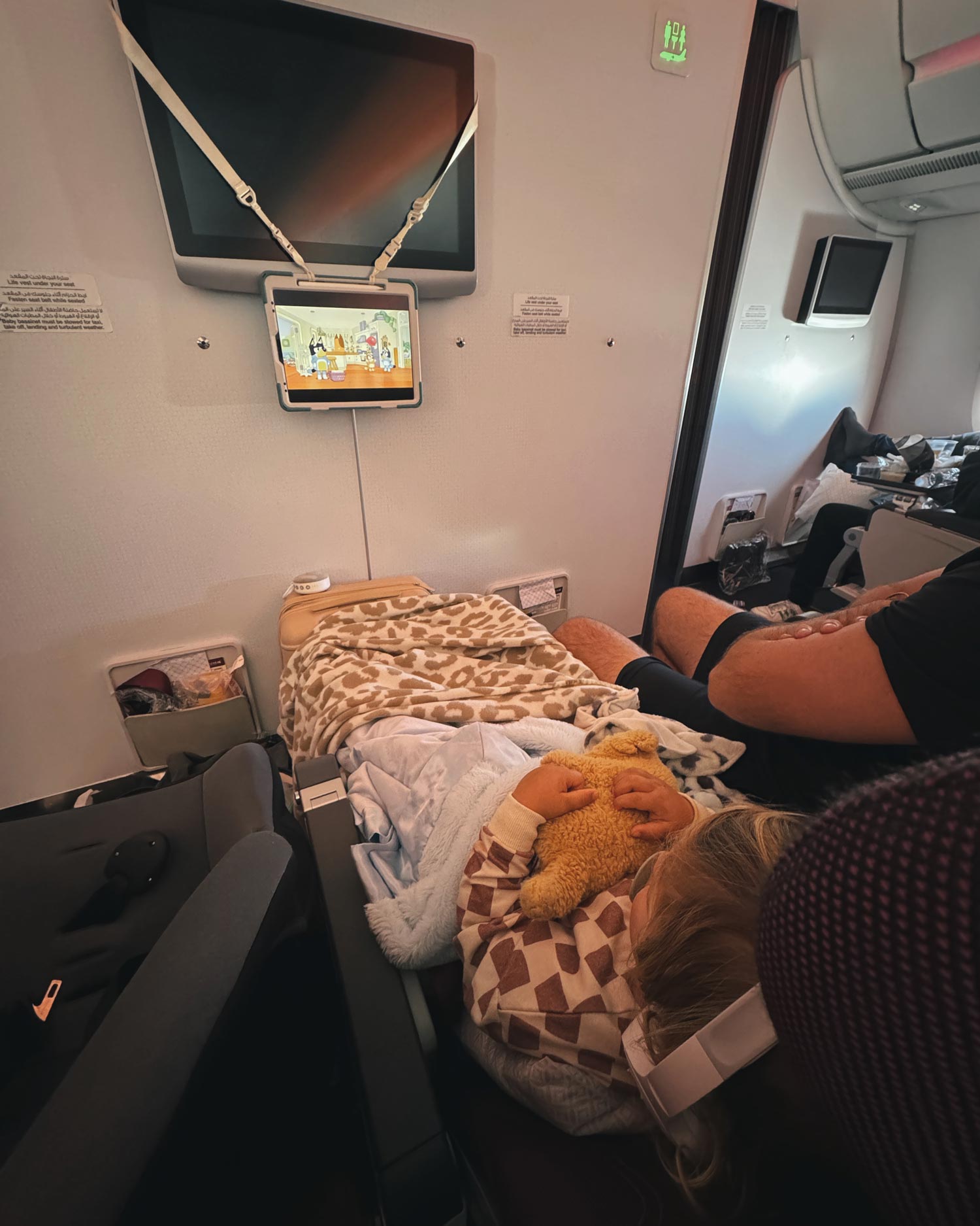 toddler watching iPad hanging from a shockproof case on airplane , while lying on a toddler airplane air mattress cuddling a stuffed puppy