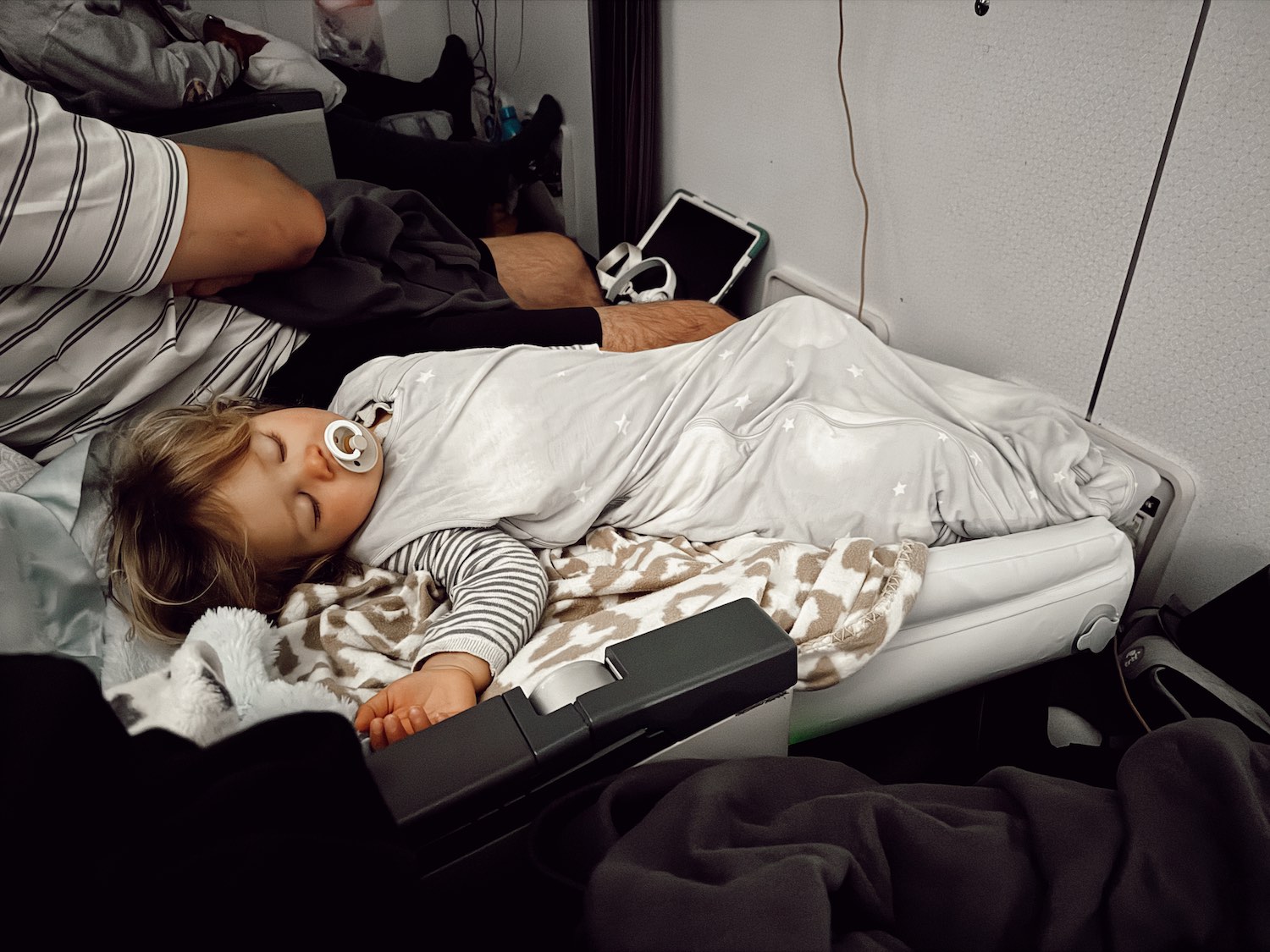 Little toddler boy sleeping in plane on inflatable mattress with pacififier and blankets