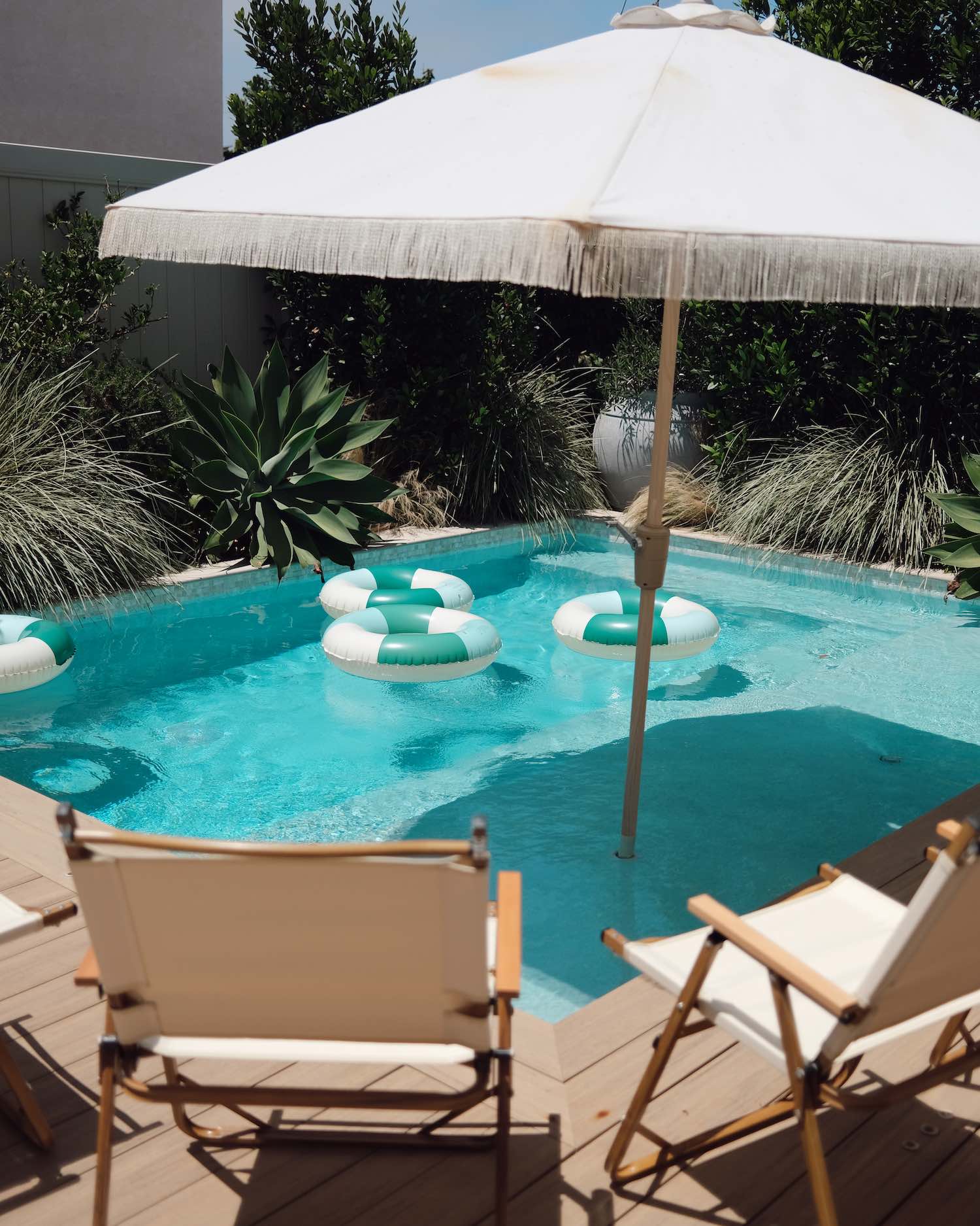 Backyard pool with lounge chairs, a large white sun umbrella and pool toys striped with white and blue colors