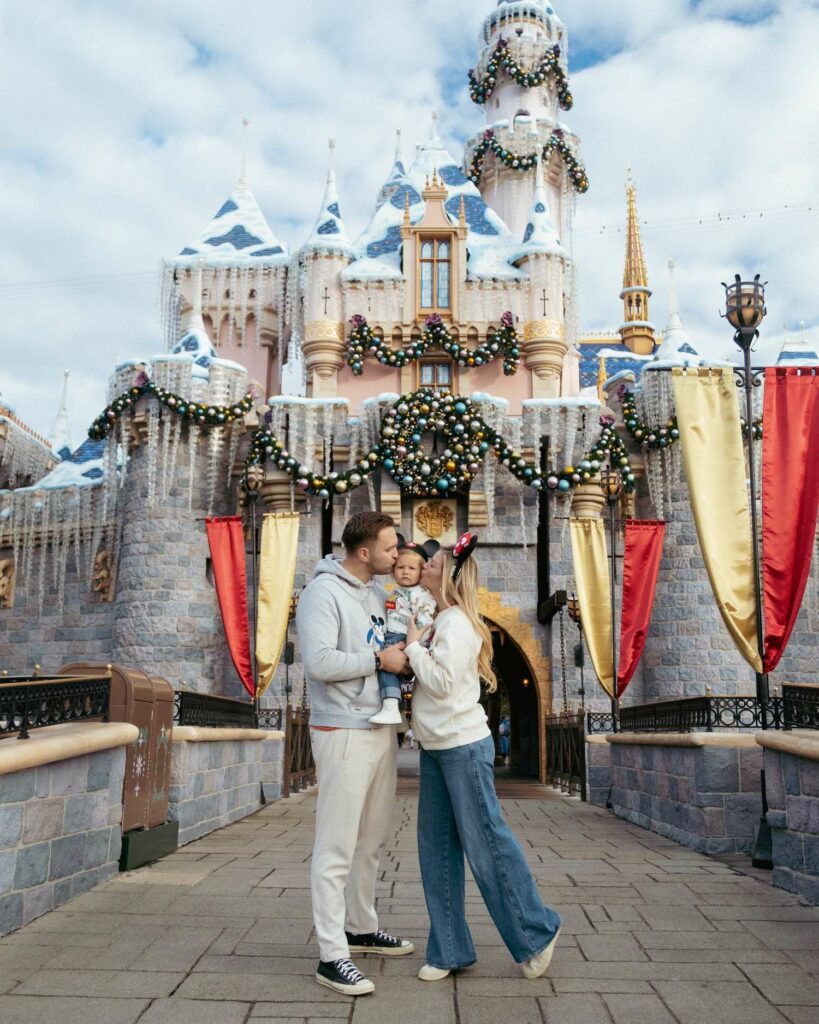 Mom and Dad kissing little boy in front of Sleeping Beauty Castle at Disneyland California