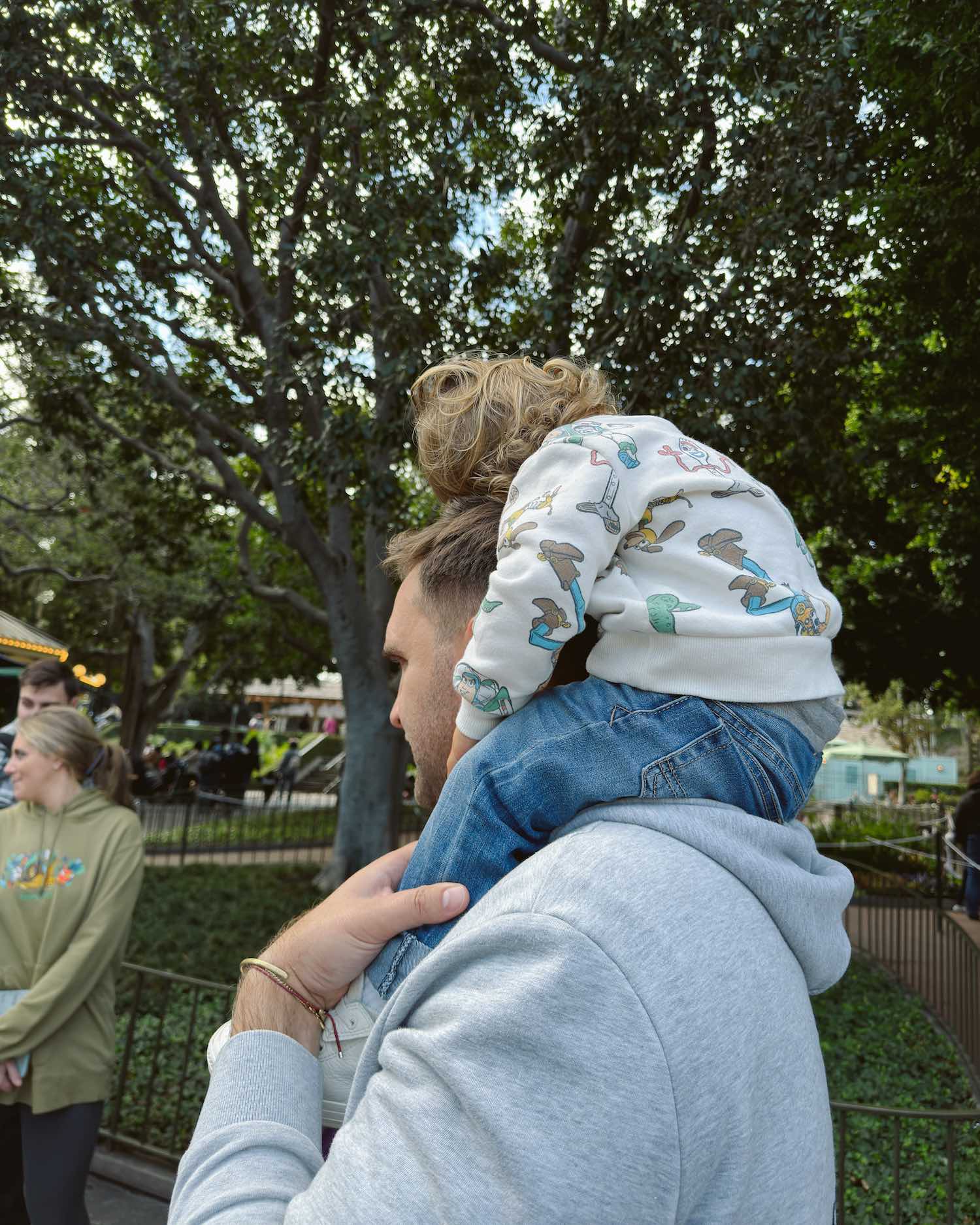 Little boy in printed Toy Story sweatshirt resting his head on his dad's as he sits on his shoulders